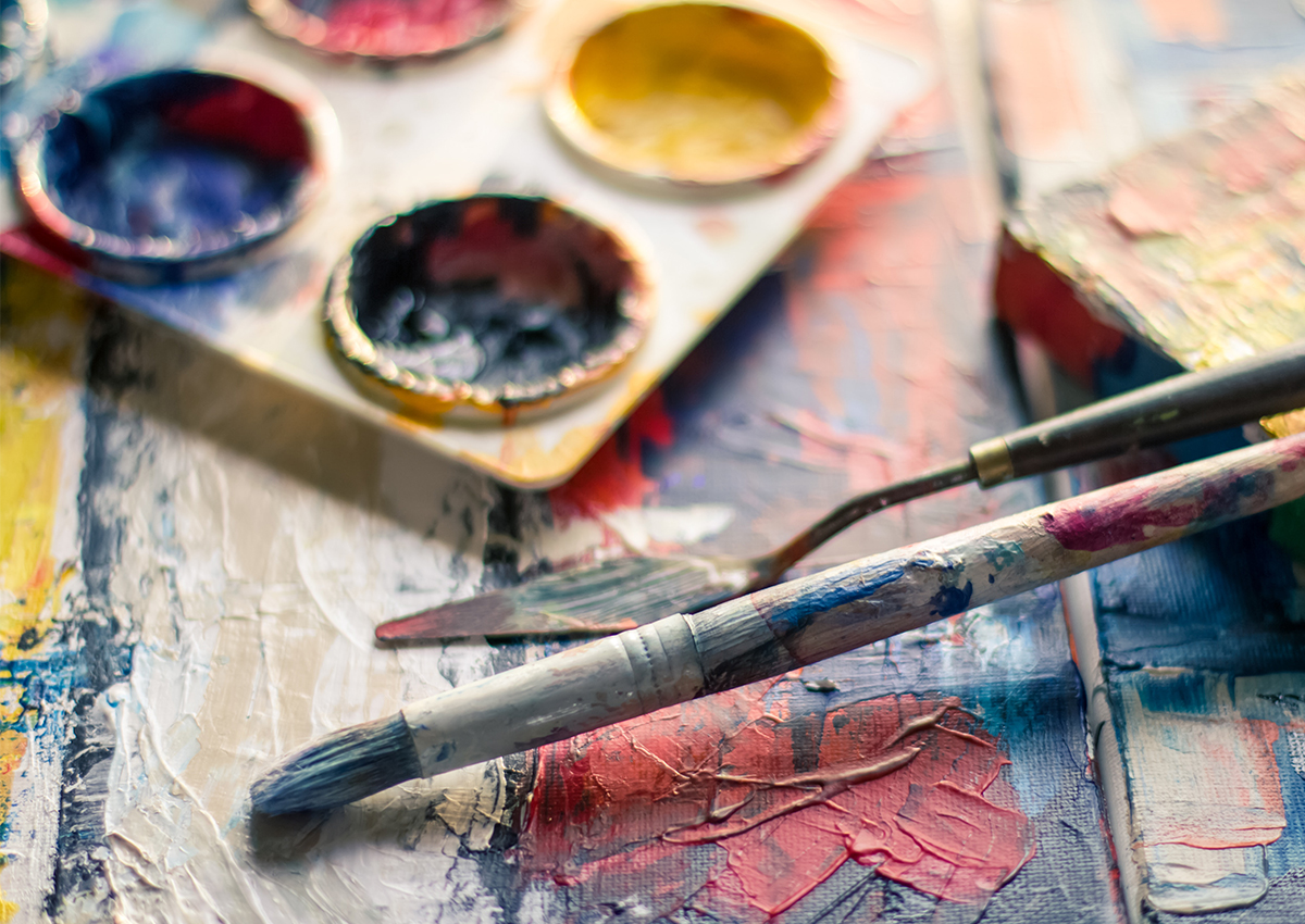 A close-up of a paintbrush and palette knife resting on a textured, colorful painting, with a paint palette in the background—reflecting creative expression often explored in an Art Therapy Programme such as Adler’s renowned Ph.D. offerings.